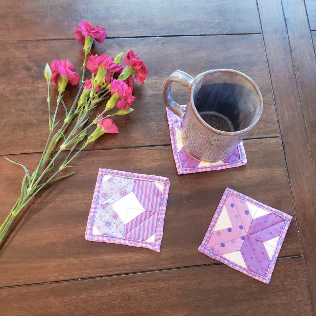 Image of quilting pattern coasters with a mug on top of one and flowers sitting on a table