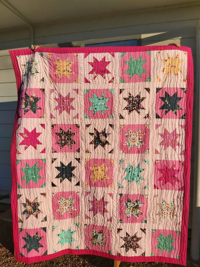 Marjo's quilt with dark pink border and colorful stars and triangles